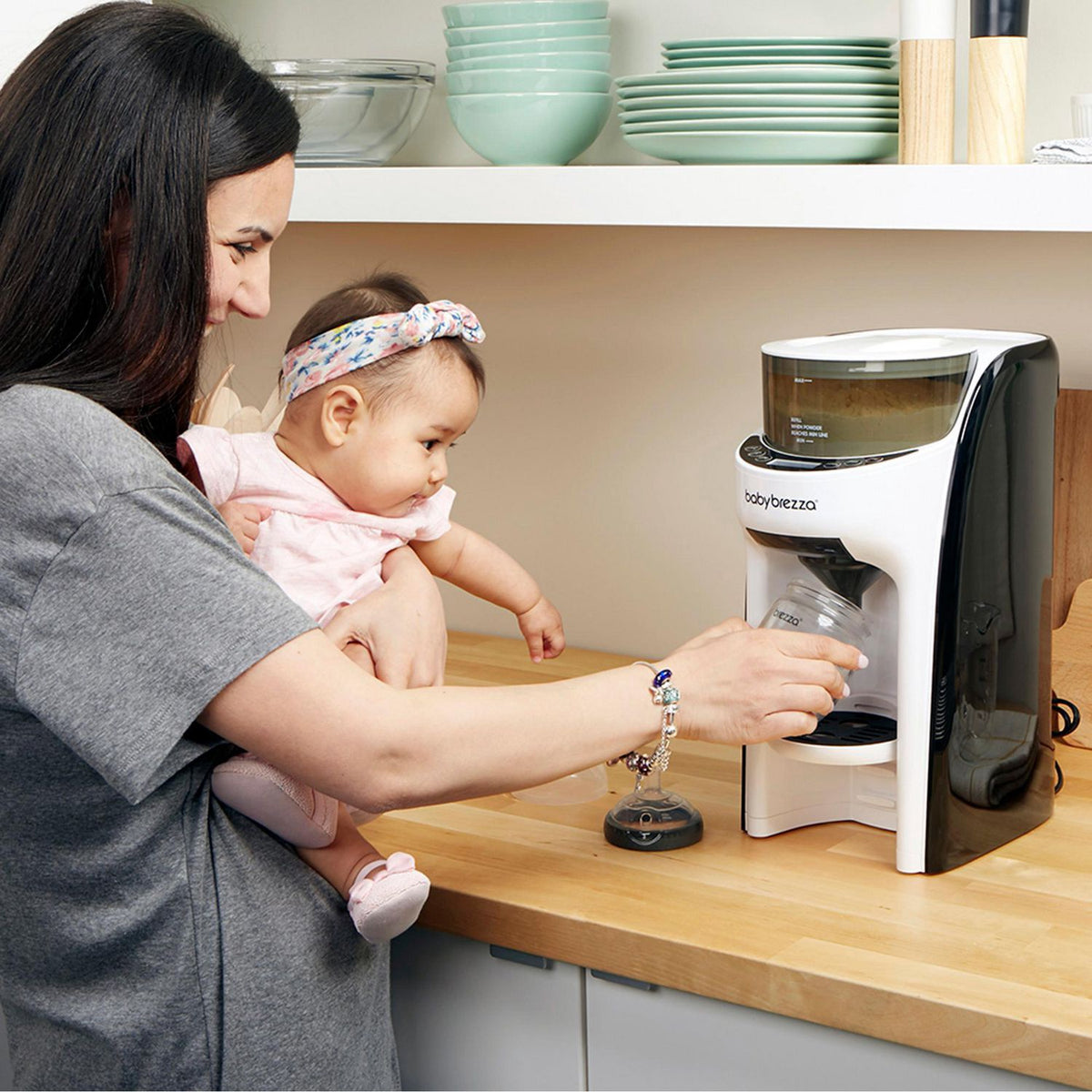 Woman holding a baby while using a coffee maker on a kitchen counter.