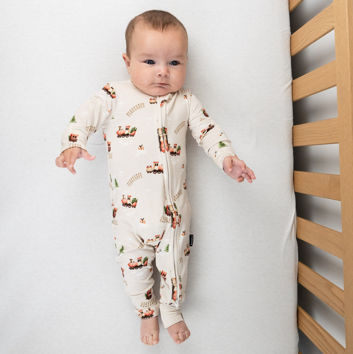 Belan.J bamboo footless sleeper with a print of red trains carrying Christmas trees and gifts through the snow
